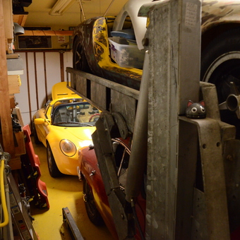 Classic Cars on Lift and Yellow Sports Car in Packed Garage - jabingb