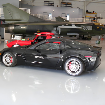 Glossy Black Corvette and Red Sports Car in Polished Garage - Bill