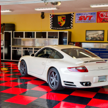 Aluminum garage cabinets with a white Porsche and black and red flooring with a car lift